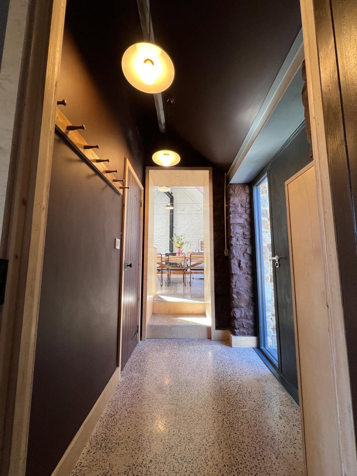 Hallway with dark walls, ply lined openings and reveals, oak peg rail and exposed stone pier