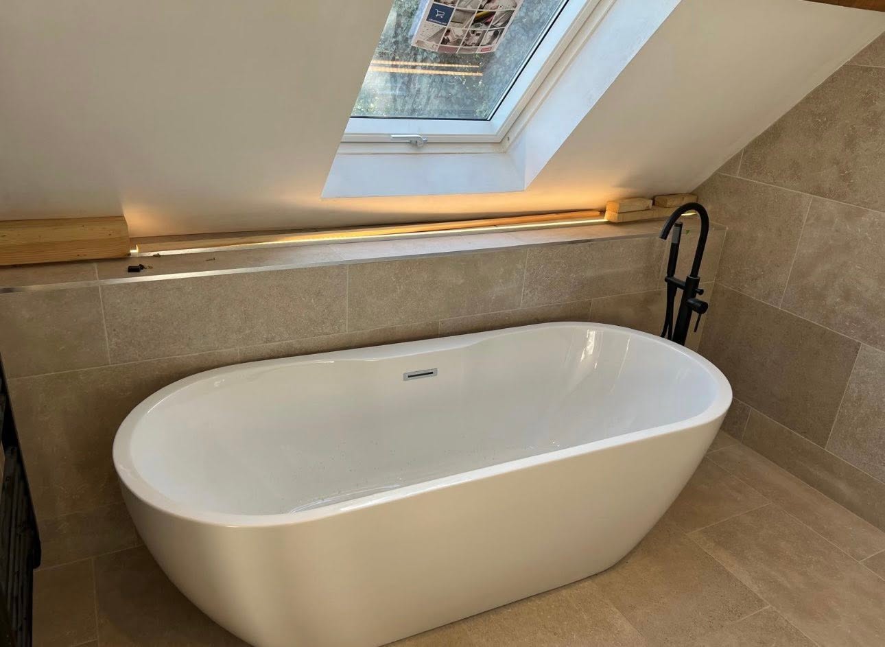Freestanding bath under Velux with concealed LED strip and stone tiling