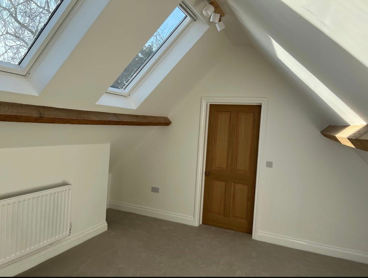 Loft conversion bedroom with vaulted ceiling, exposed timber beams and Velux rooflights