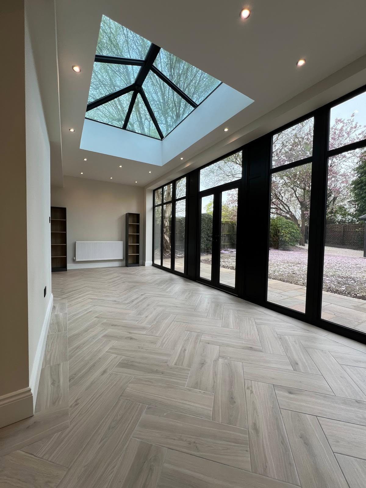 Sunroom with light grey wood herringbone floor and a black framed glass lantern roof