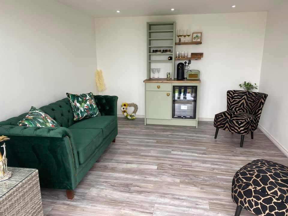 Finished interior with emerald green buttoned velvet Chesterfield sofa, animal print armchair and grey wood effect flooring