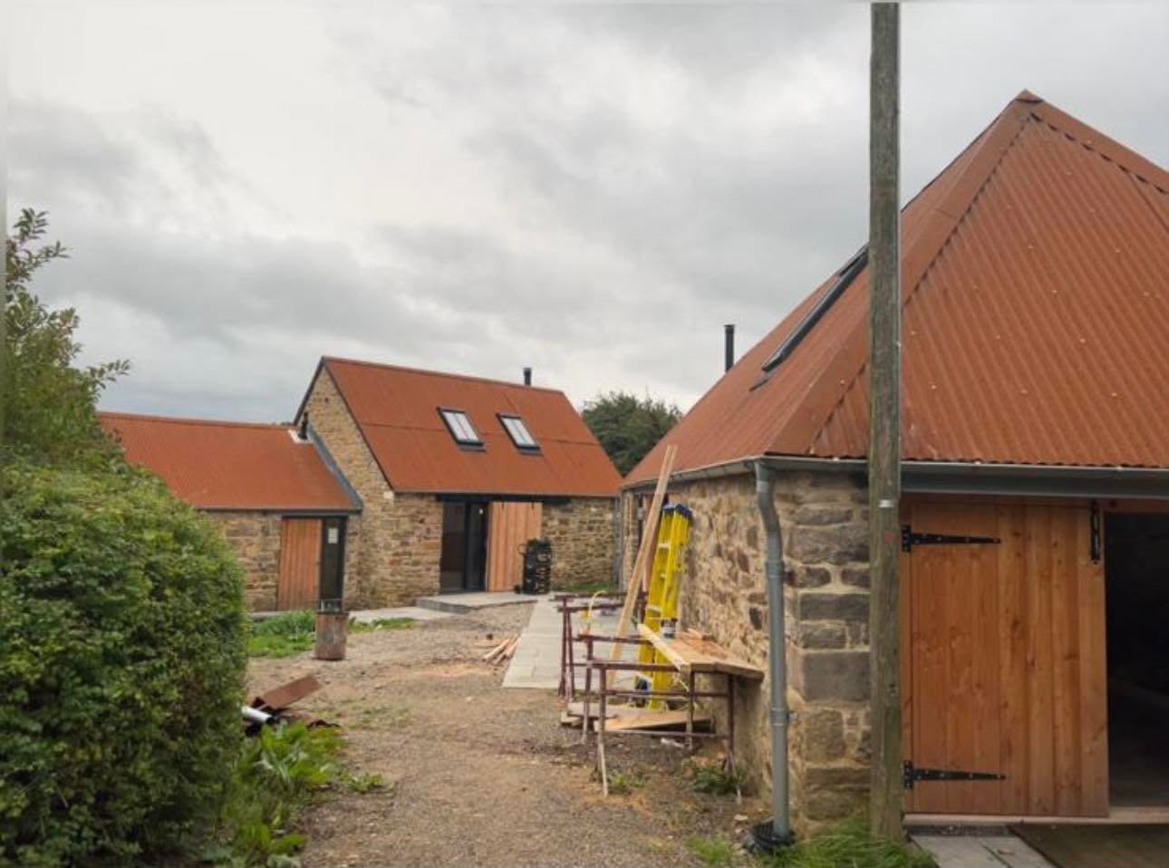 Late build stage across the yard with finished roofs, new ledged and braced barn doors and new paving