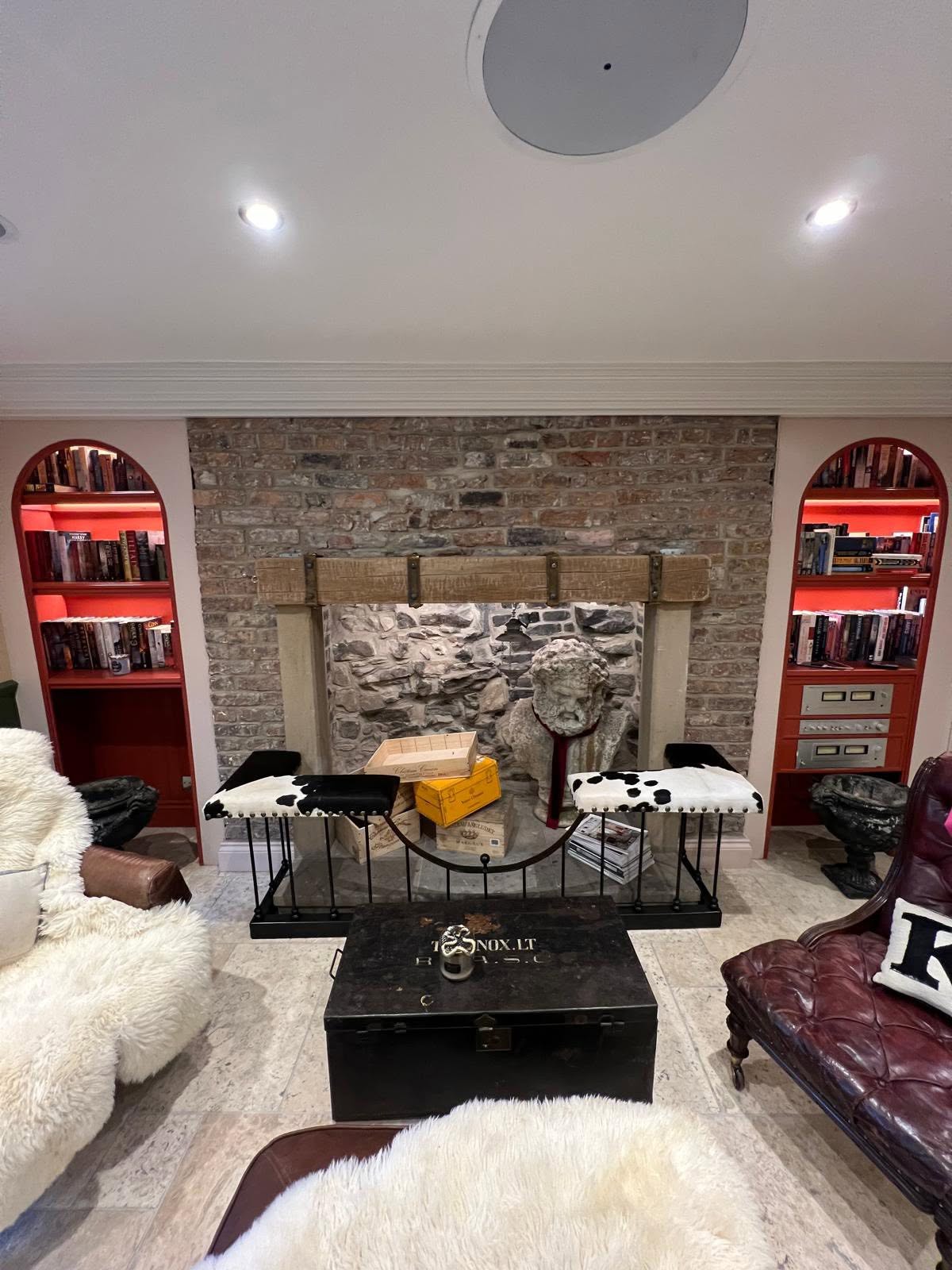 Lounge focal wall with symmetrical red arched bookcases, lit shelving and reclaimed brick fireplace
