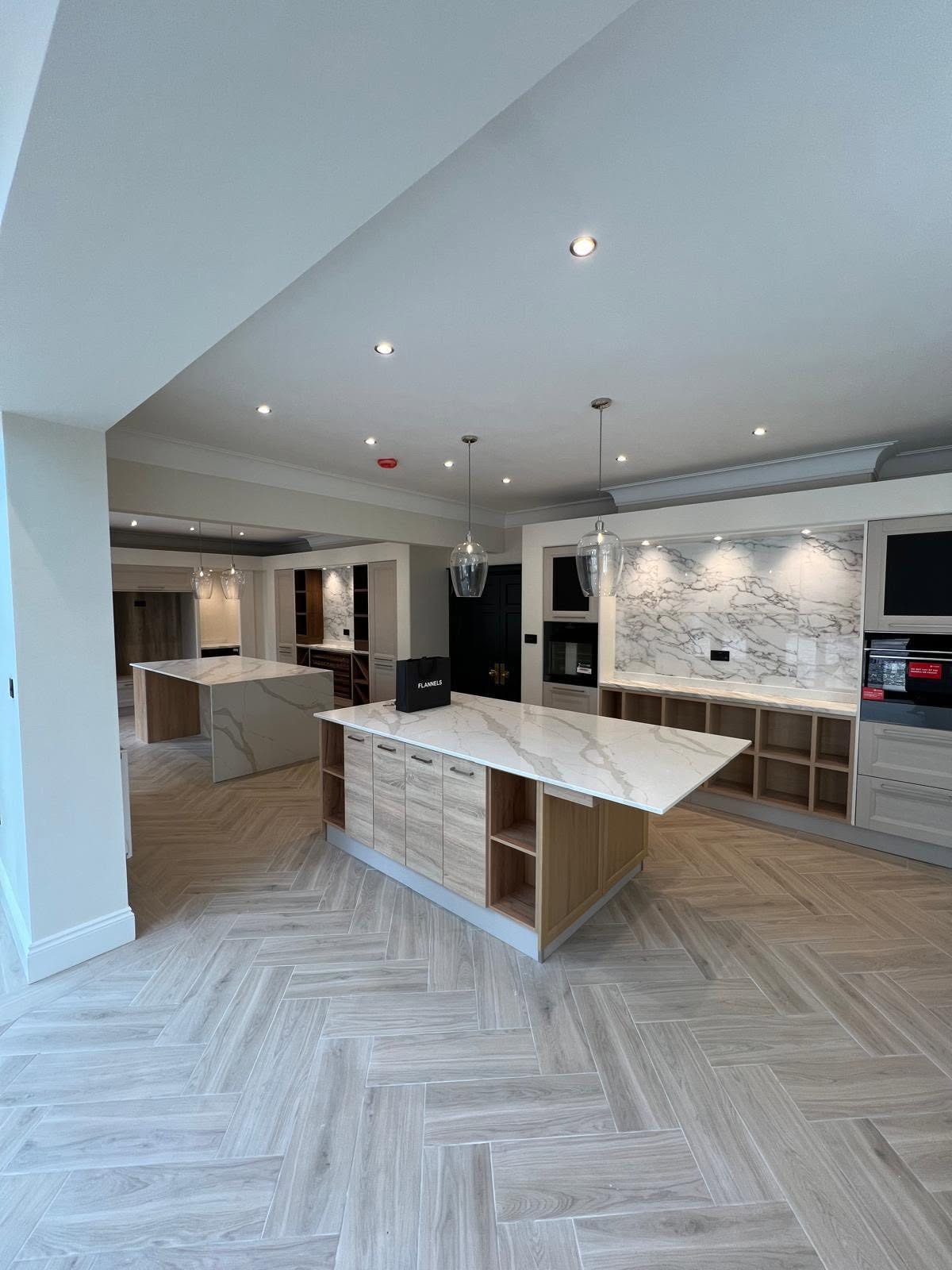 Kitchen with two matching marble waterfall islands and light wood herringbone flooring