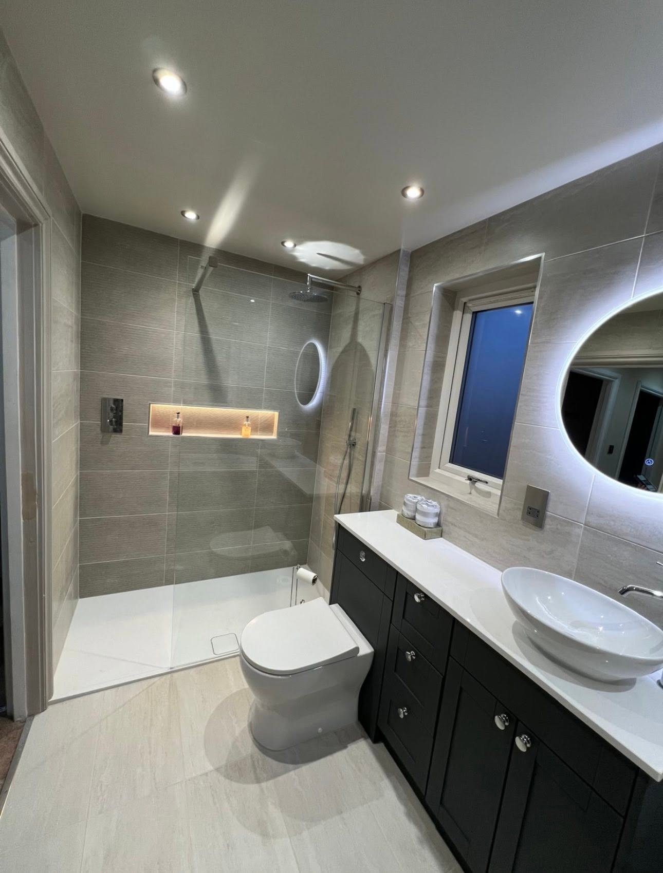 Walk in shower with low profile tray, glass screen, lit recessed niche and textured feature tiling