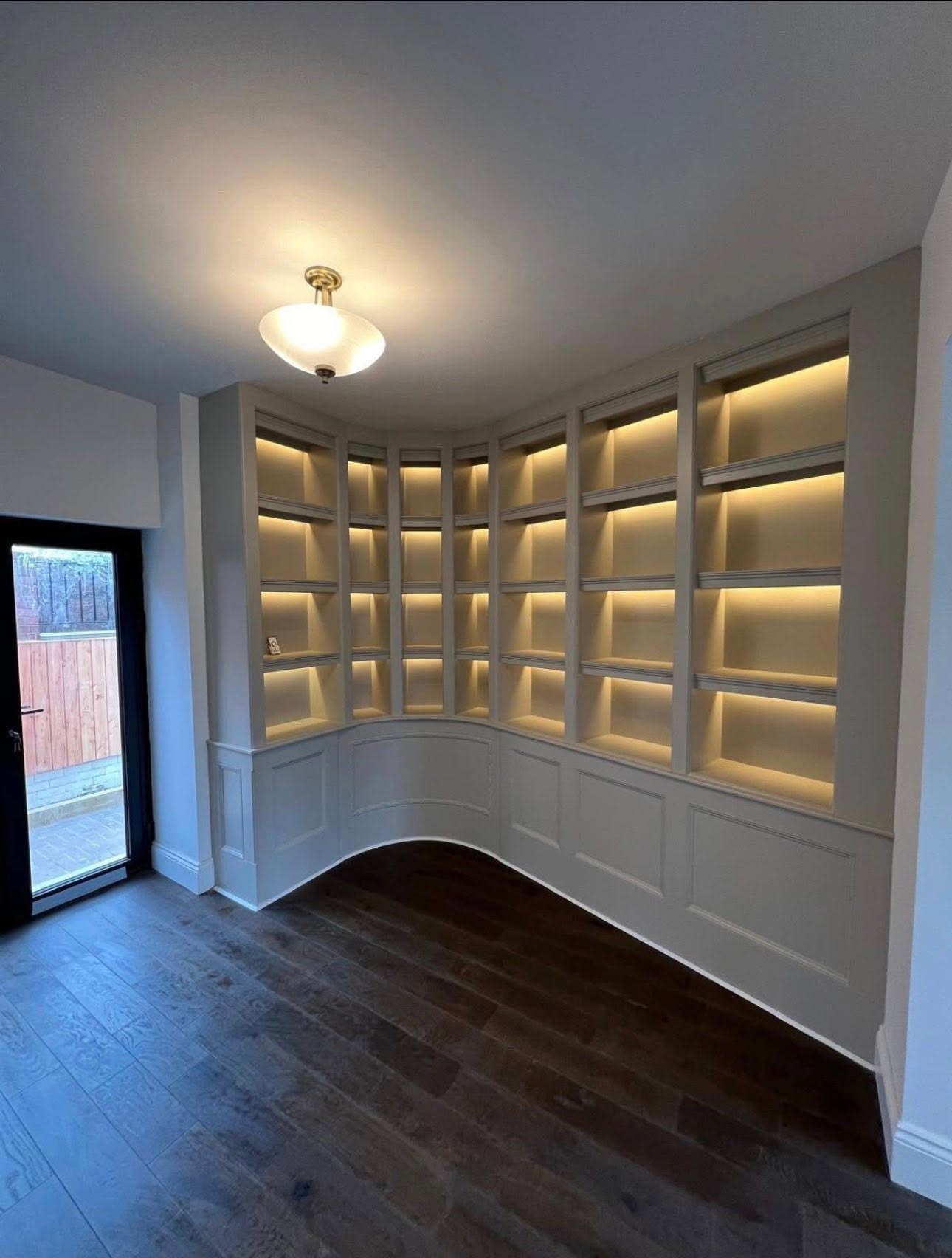 Transitional space with a curved taupe built in shelving unit and warm lighting