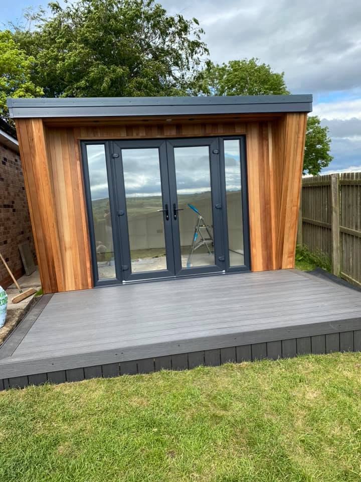 Completed garden room exterior with vertical western red cedar cladding, dark grey capping and anthracite French doors onto composite decking