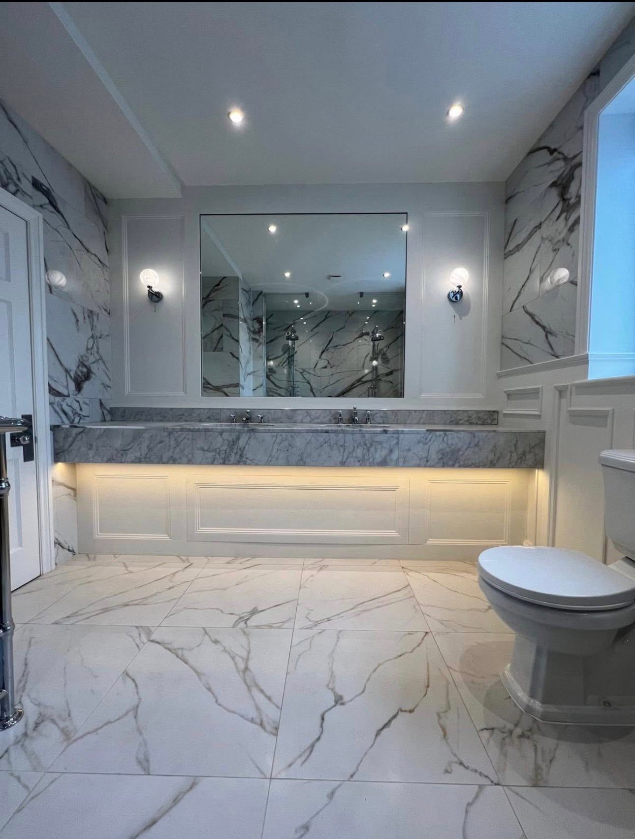 Wide view of a marble tiled bathroom with large mirror and vanity
