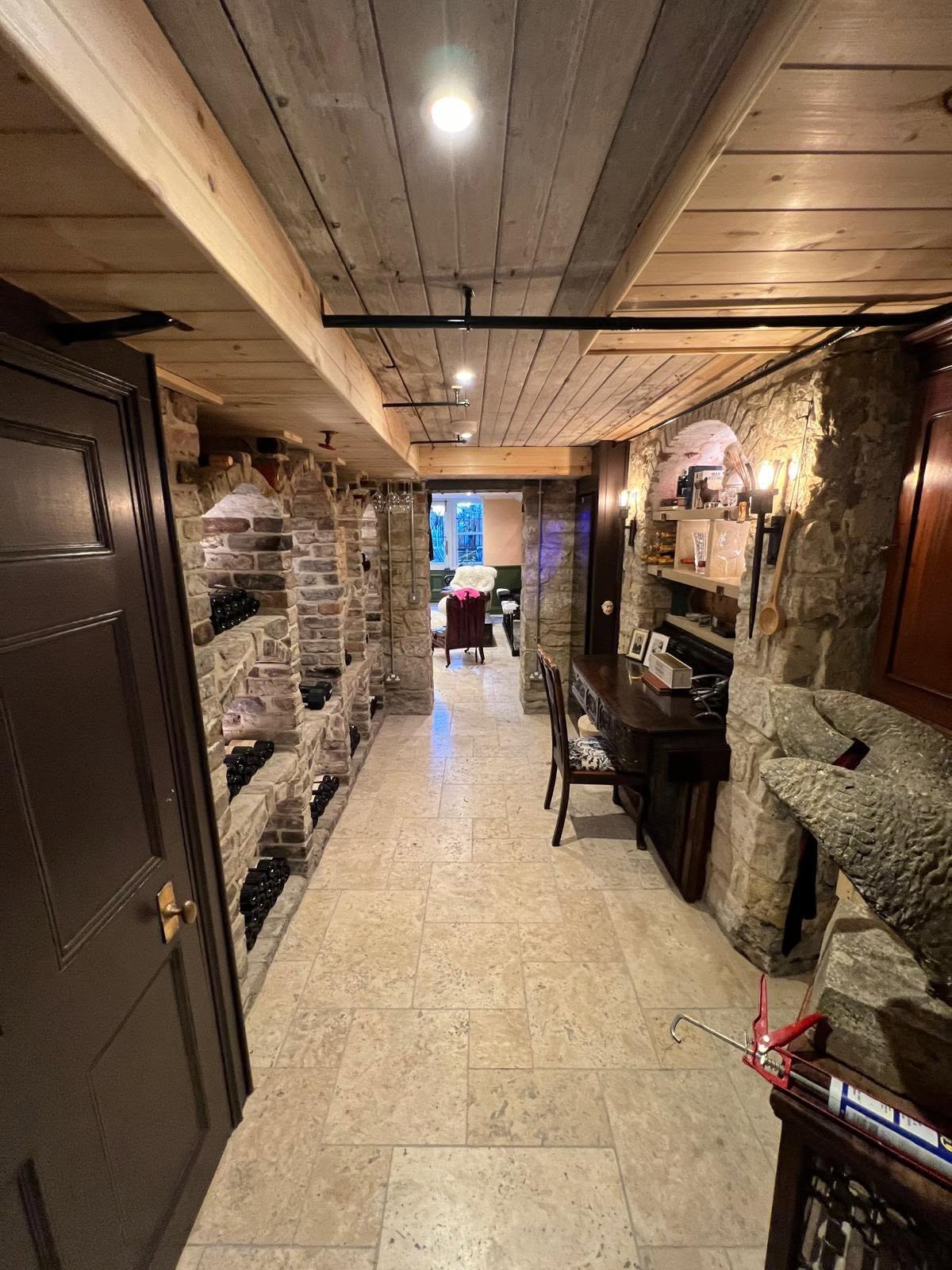 Cellar corridor with stone bottle niches one side and stone shelved desk nook with sconces the other
