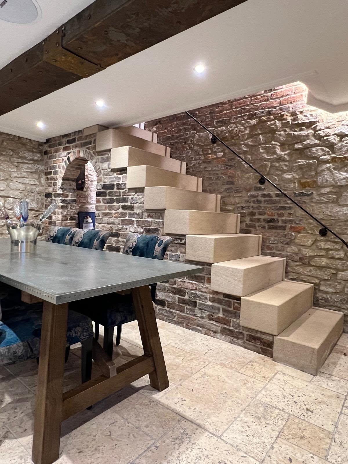 Close view of cantilevered stone treads against reclaimed brick with concealed cornice lighting and arched niche behind