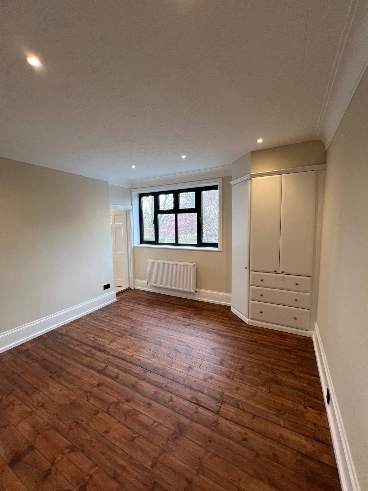 Bedroom with dark wood floor, cream walls and a corner fitted wardrobe