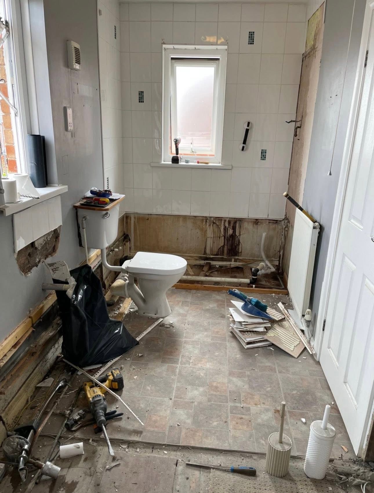 Strip out in progress with tiles and bath removed, exposed walls and pipework