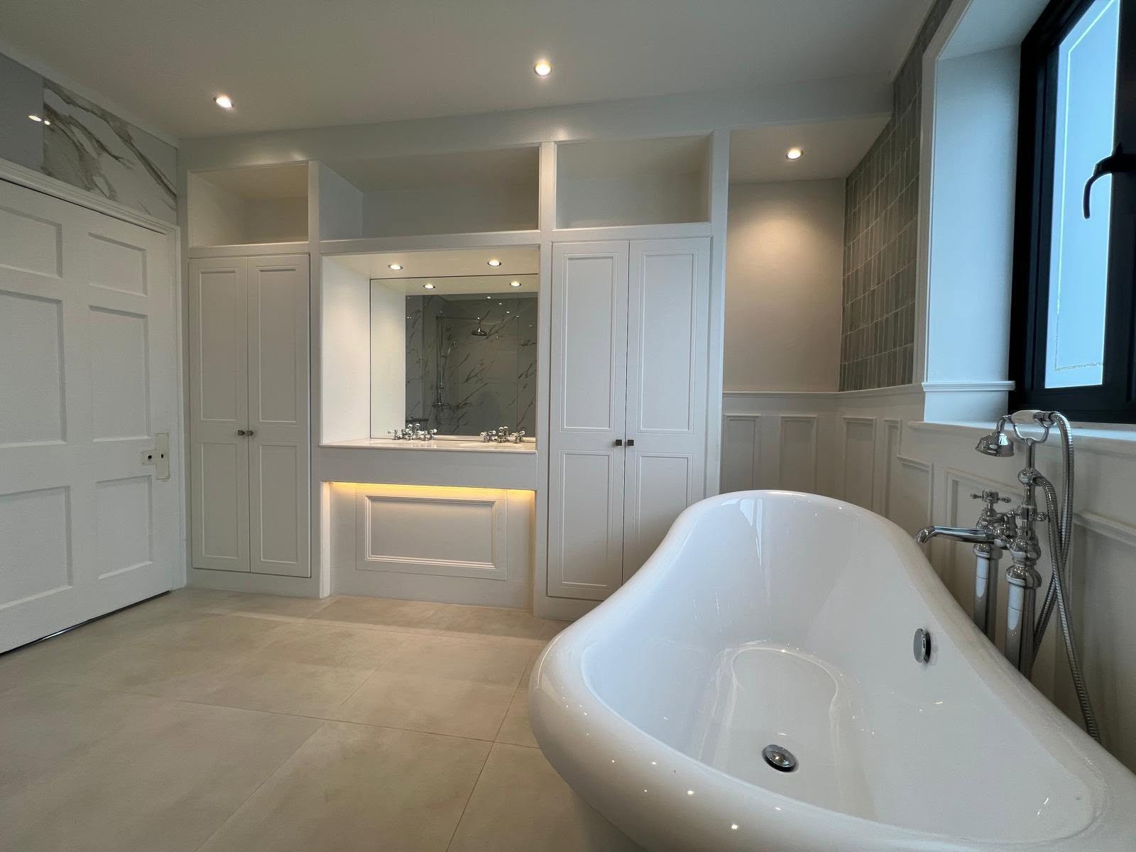 Bathroom with fitted white cabinetry, integrated lighting and bath