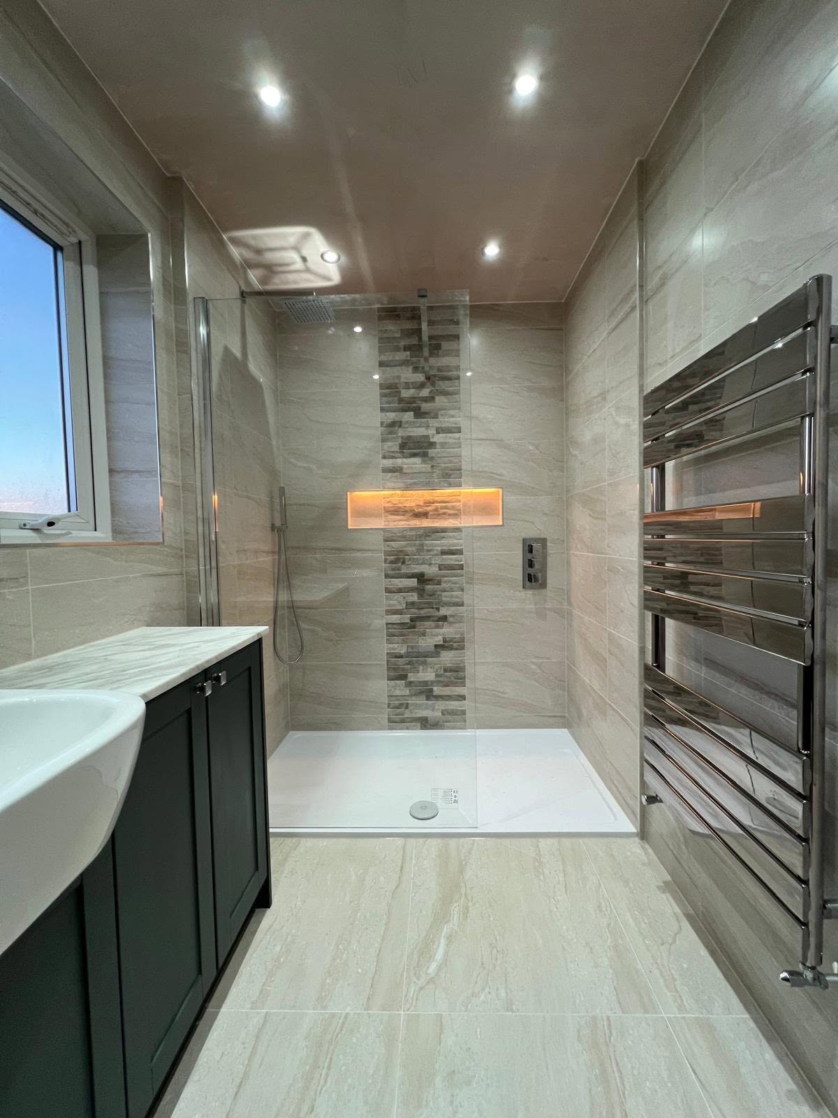 Along the wet room showing shower enclosure with glass screen, lit niche and sculptural chrome towel radiator