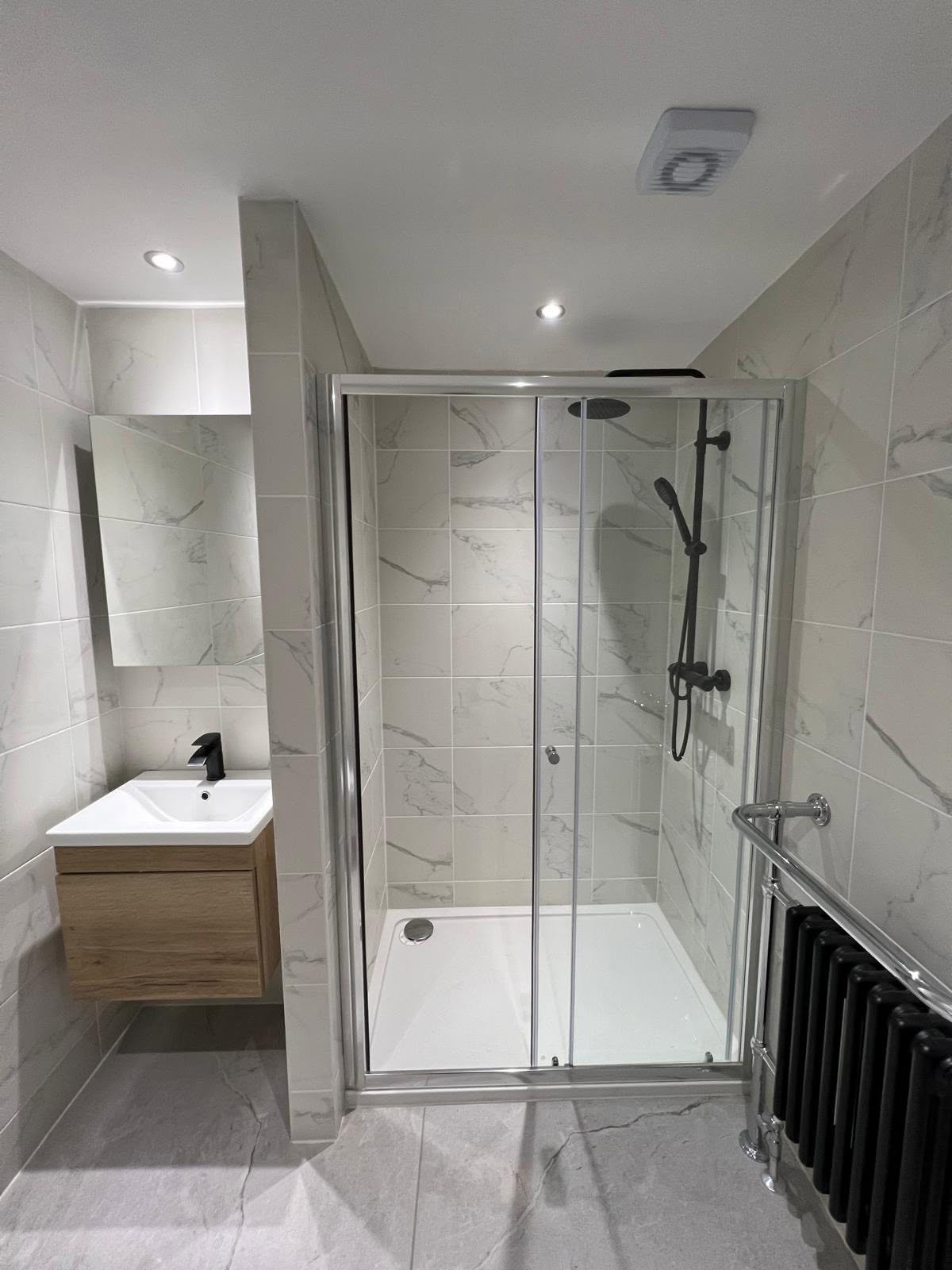 Shower enclosure with sliding chrome door, black column radiator and oak vanity beyond