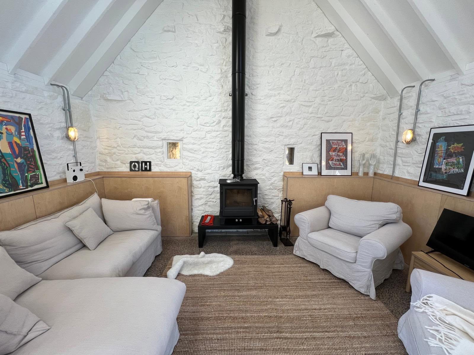 Snug end with white painted stone gable, wood burner, ply panelling, bulkhead wall lights and jute rug