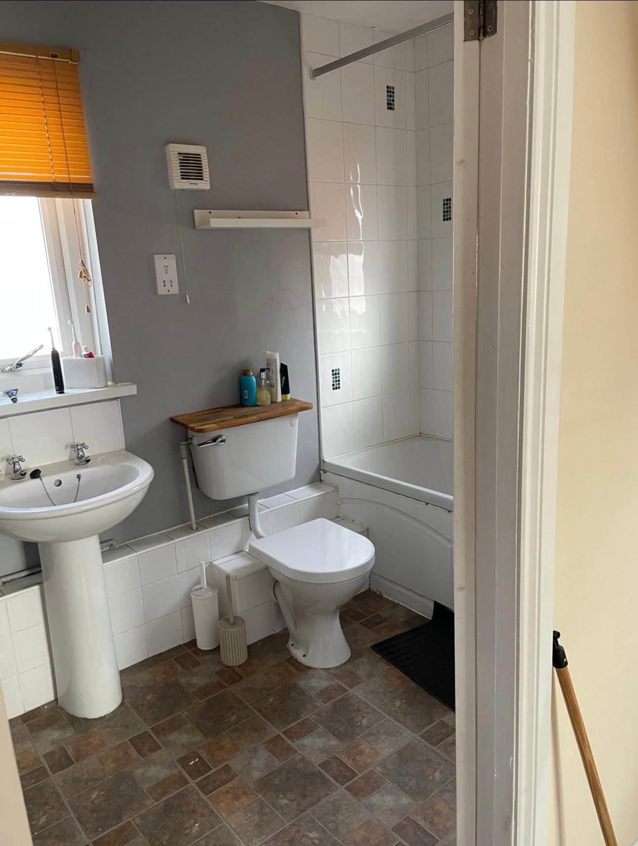 Before: dated bathroom with pedestal basin, close coupled WC, panelled bath with shower over and worn vinyl floor
