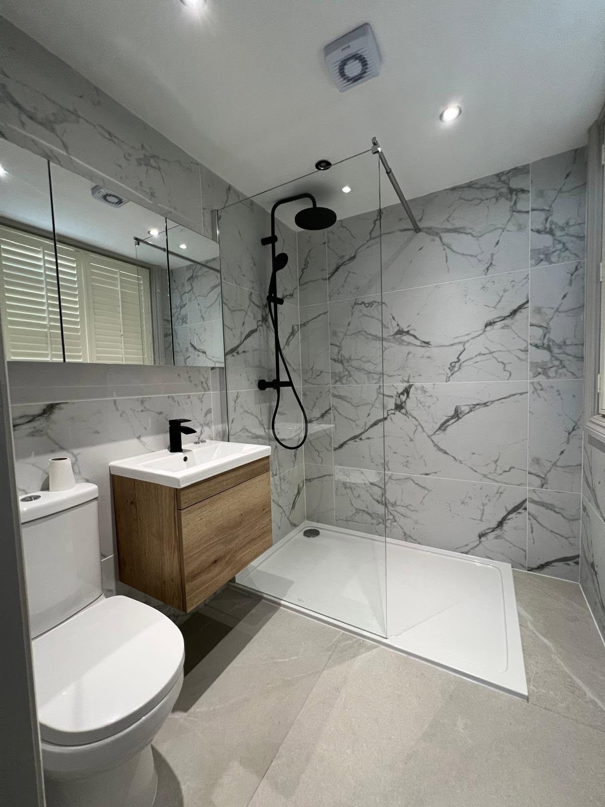Marble effect porcelain shower room with matt black rain shower, oak wall hung vanity and mirrored cabinet