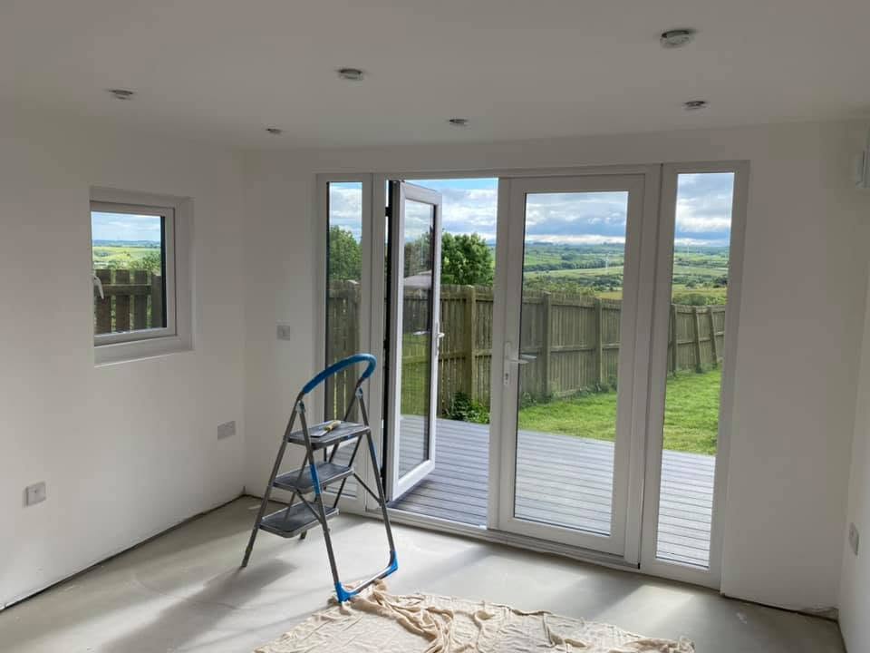 Interior during finishing with plastered white walls, recessed downlights and white French doors onto the deck