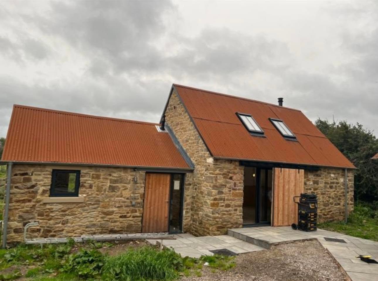 Completed exterior with repointed rubble stone, terracotta roof, black framed glazing and larch sliding barn doors