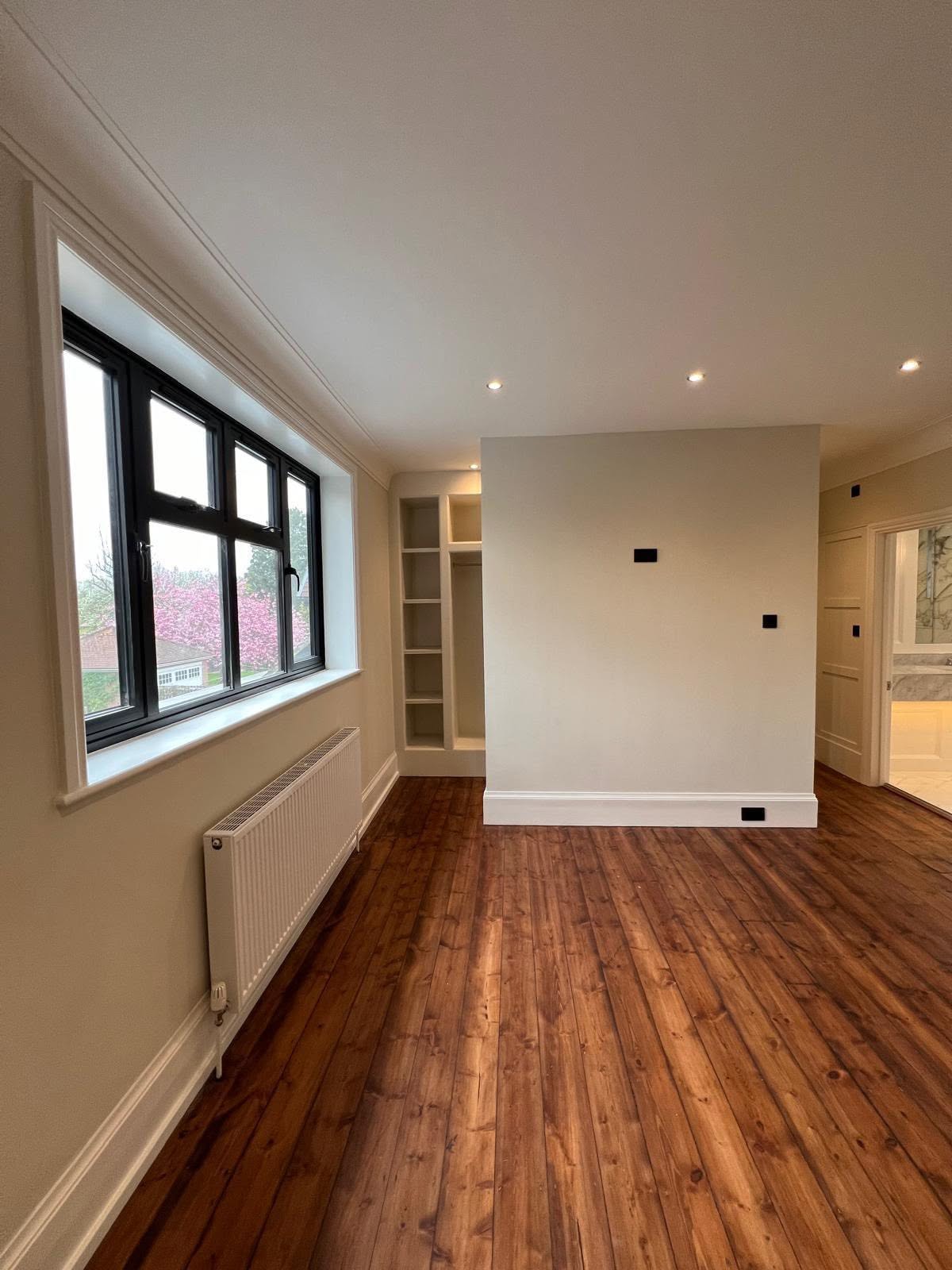 Room with dark wood flooring, cream walls and a large black framed window