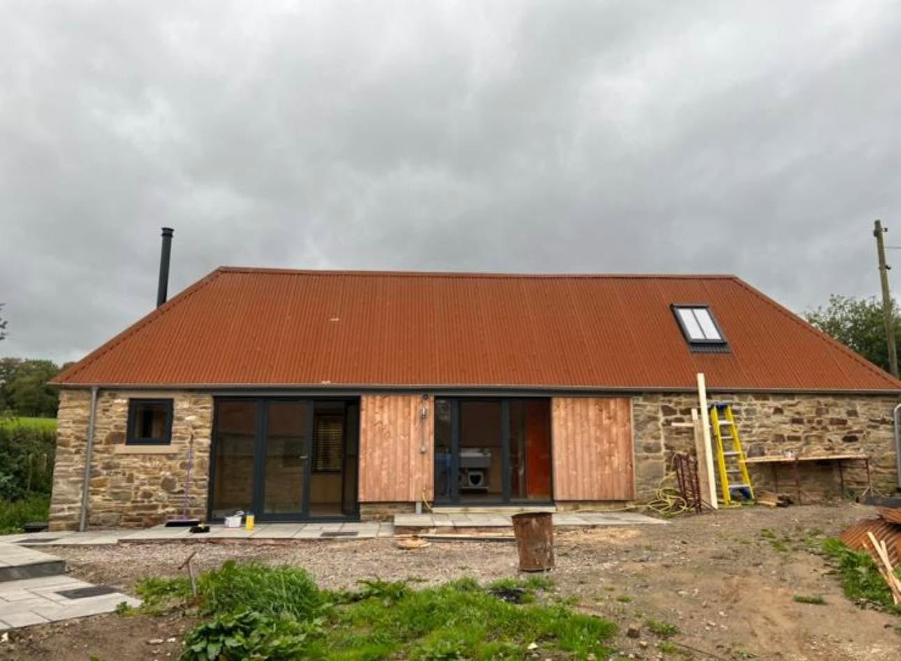 Long elevation with sliding timber shutters over glazed openings and stone walls