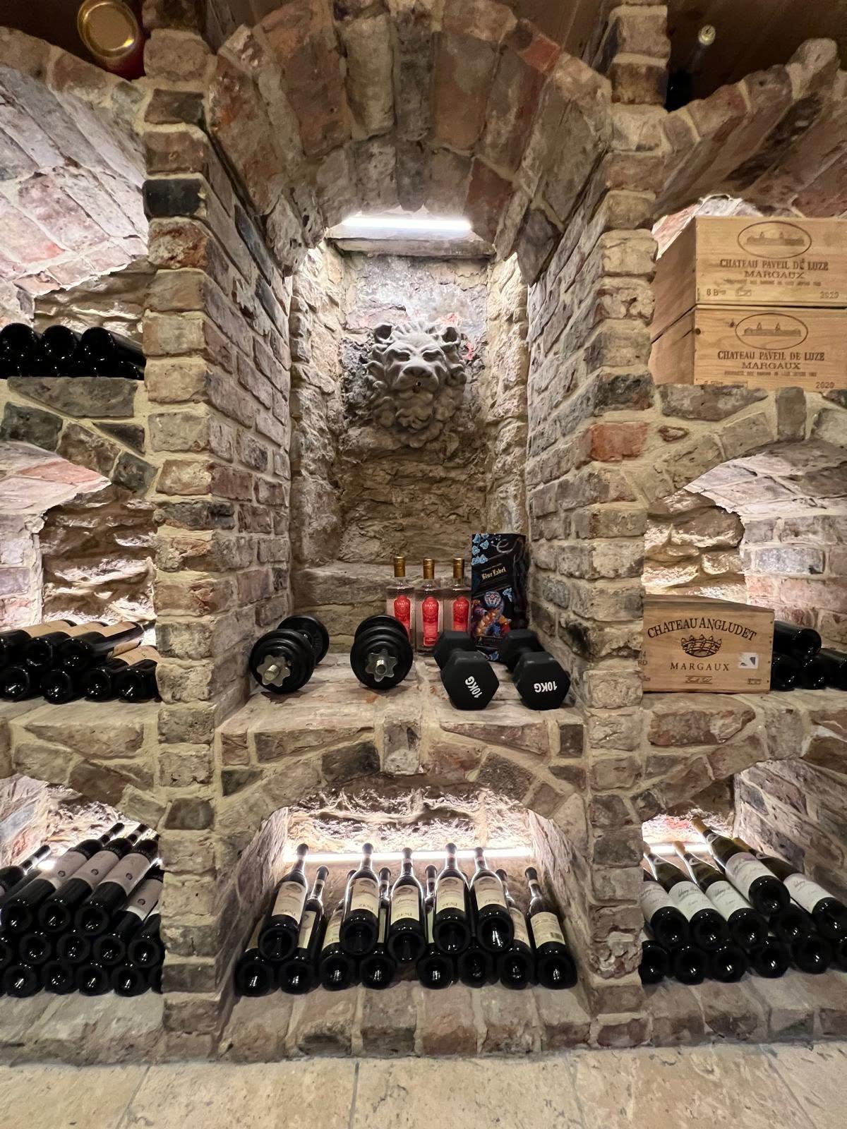 Wine cellar centre bay detail with carved stone lion mask in the arched recess and LED lit bottle shelves