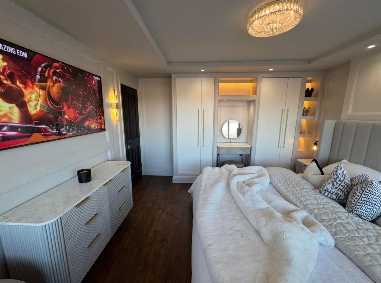 Fitted wardrobe run with brass bar handles, lit dressing table nook with round mirror and lit display shelving