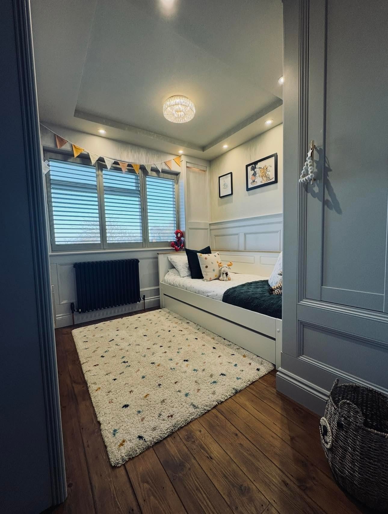 Child's bedroom from the doorway with feature ceiling, bay shutters, cast iron radiator and fitted wardrobe elevation