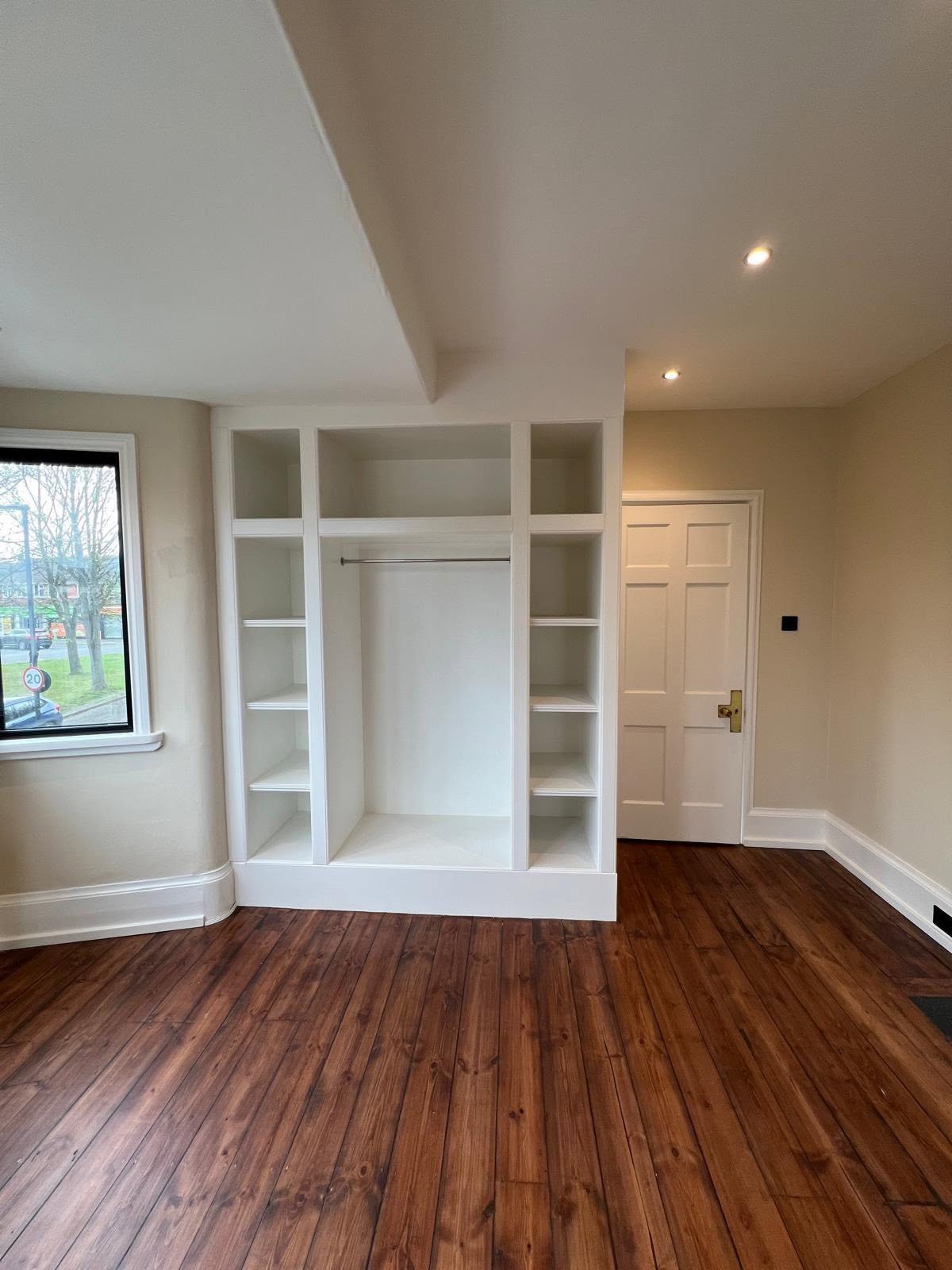Fitted closet with dark reddish brown wood floor, white open shelving and chrome rod