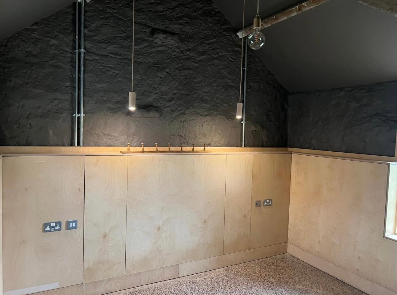 Interior with black painted stone gable, birch ply panelling, timber peg rail and terrazzo style floor