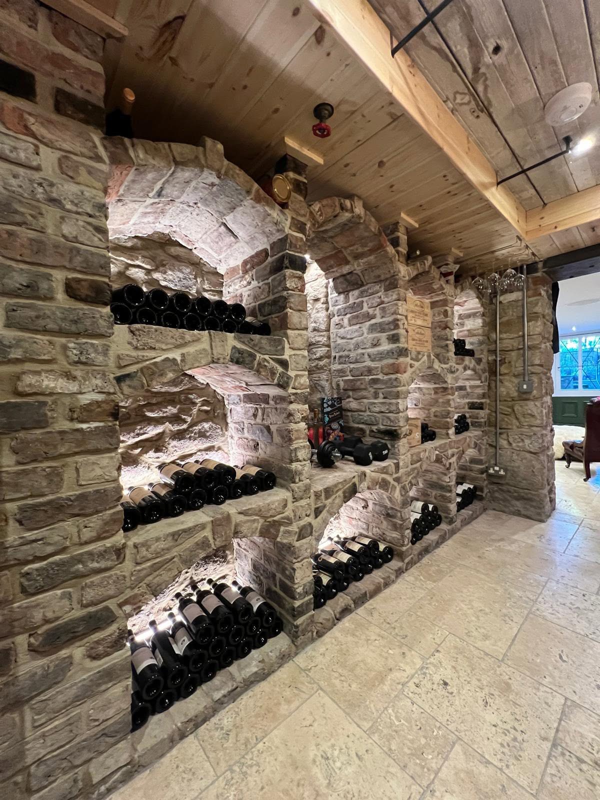 Wine cellar wall with hand-built brick and stone arched bottle niches with concealed LED strips