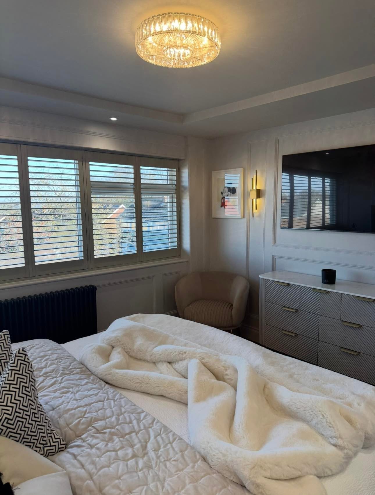 Master bedroom bay window with shutters, feature ceiling perimeter, brass sconce and fluted chest with marble top