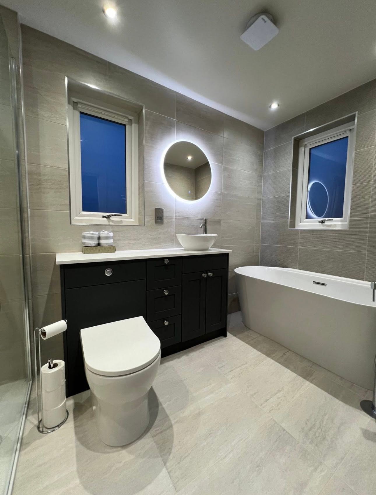 Completed grey bathroom with dark shaker vanity, quartz top, counter top basin and backlit round mirror