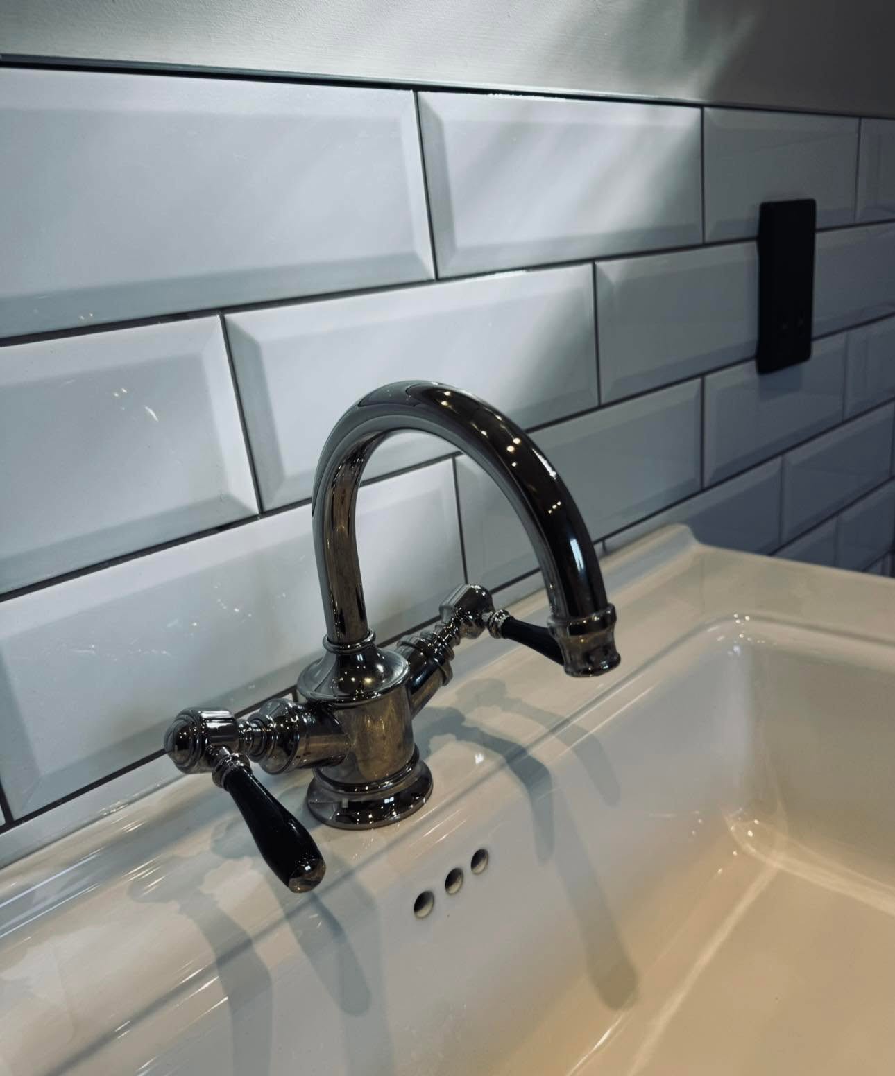 Traditional black lever basin tap on the ceramic basin against bevelled metro tiles