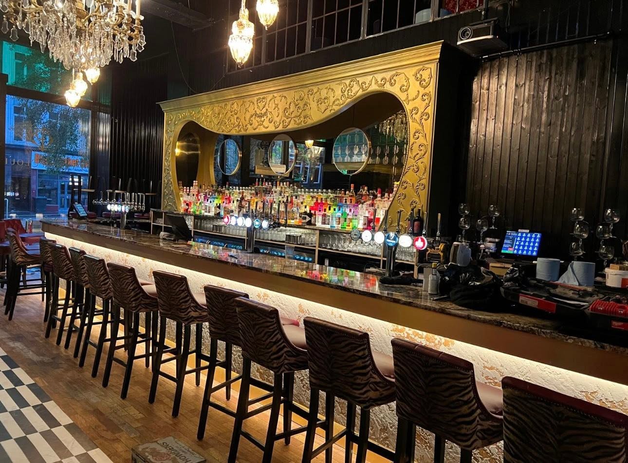 Bar counter with polished marble top, illuminated textured front and tiered liquor display in a carved gilt frame