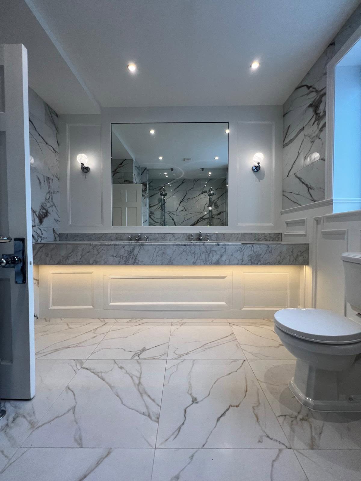 Marble tiled bathroom with backlit vanity mirror