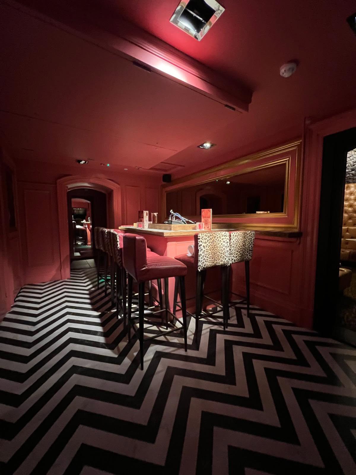 Lower bar counter with leopard and leather stools, gilt mirror and chevron floor