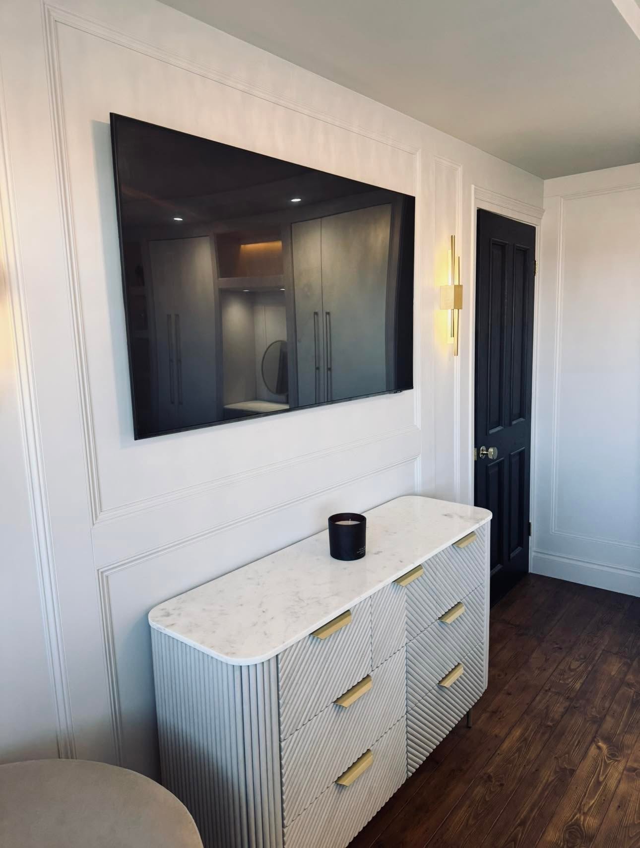 Media wall detail with TV recessed flush into the panelled wall, brass linear sconce and fluted marble topped chest