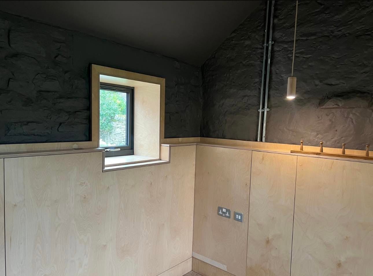 Interior detail with black painted stone walls, birch ply joinery and deep ply lined window reveal