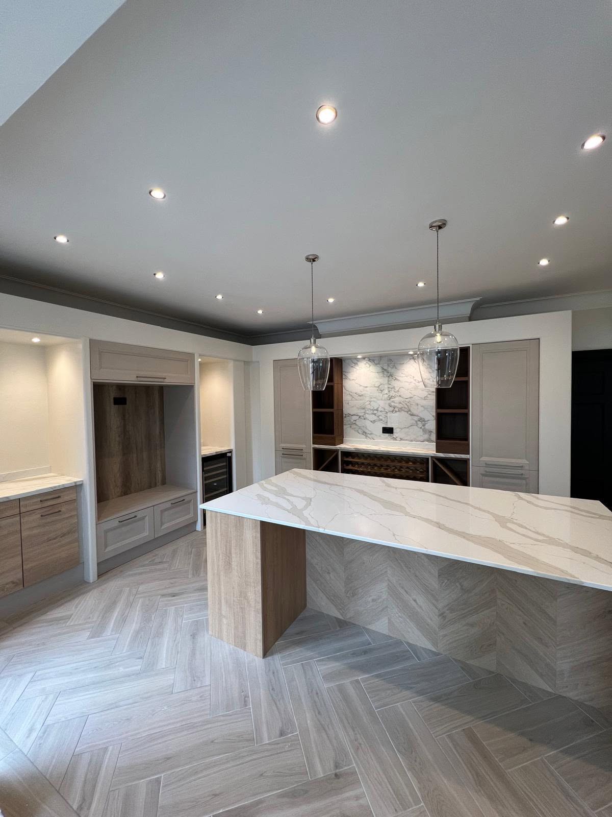 Kitchen and bar area with herringbone floor, marble island and beige cabinetry