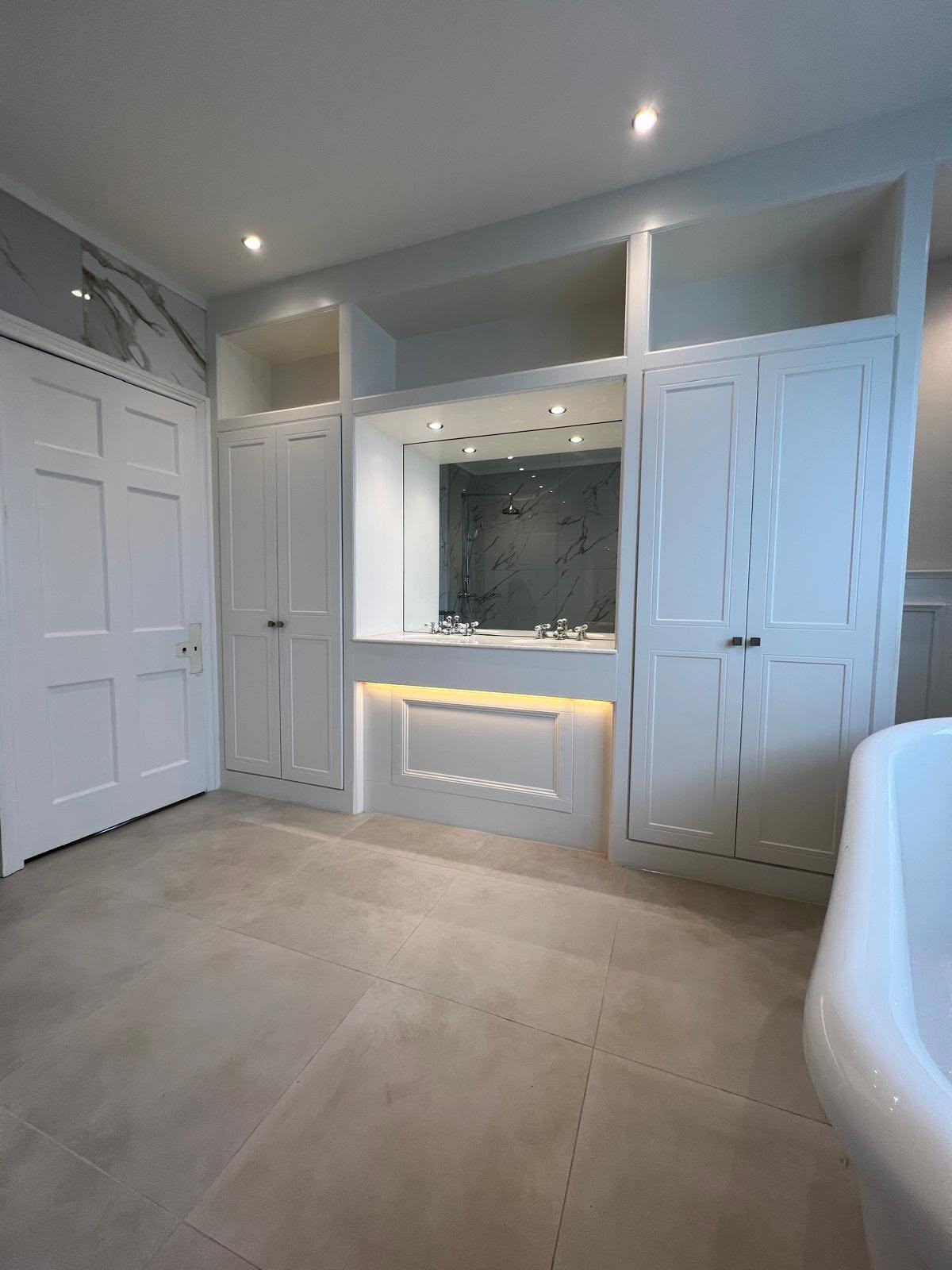 Symmetrical white built in vanity with integrated storage, under counter lighting, chrome fixtures and freestanding bathtub