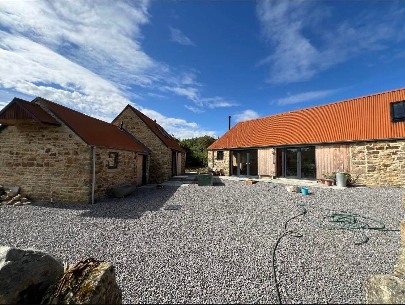Completed courtyard in sun showing three barn ranges, terracotta roofs, larch cladding and sliding shutters