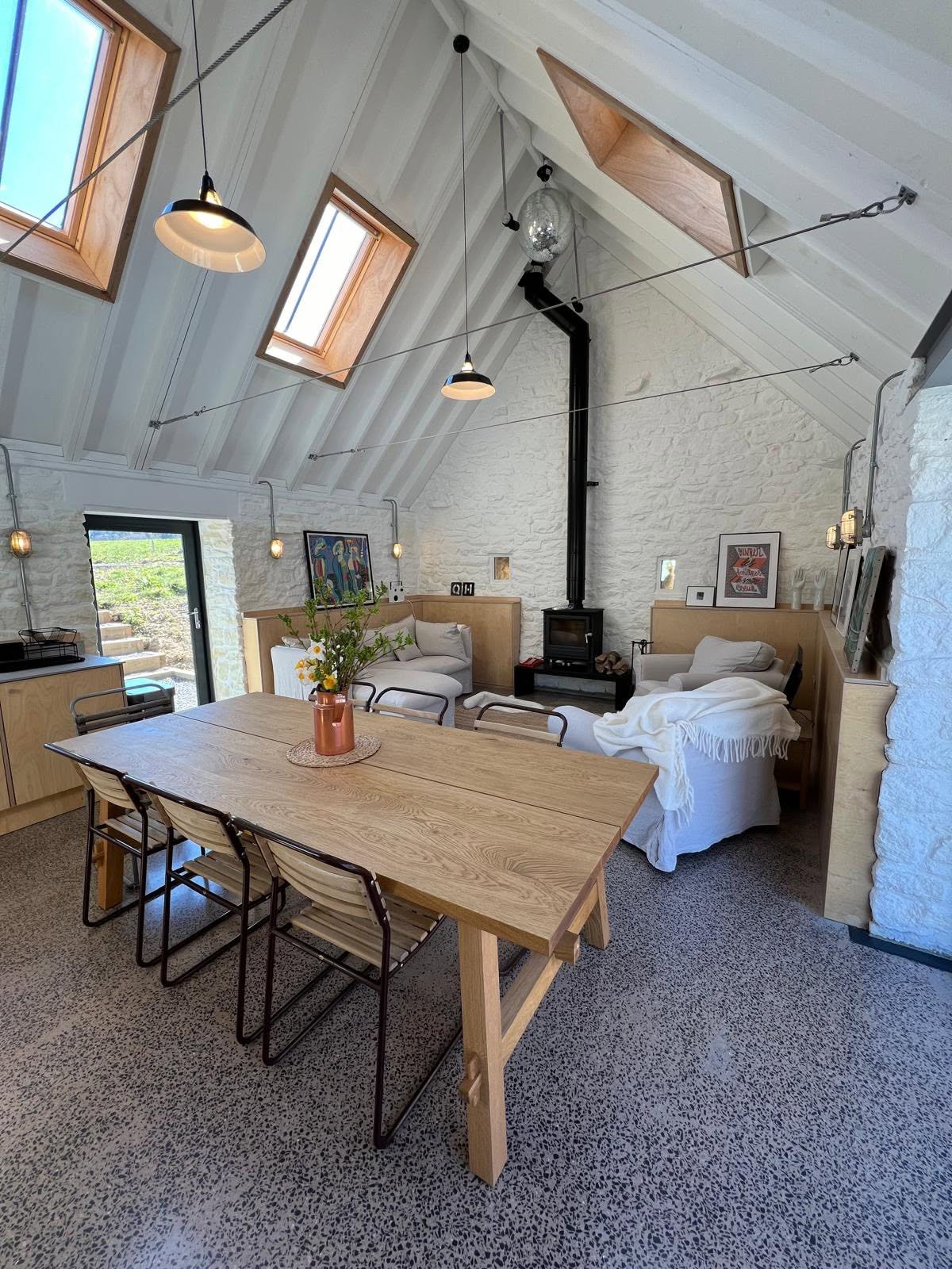 Dining and sitting zone with black pendants, mirrorball, stove and stone reveal to the glazed door