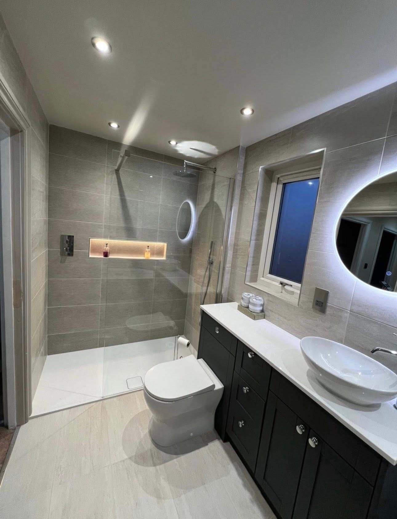 Shower room with dark vanity, vessel basin and backlit round mirror