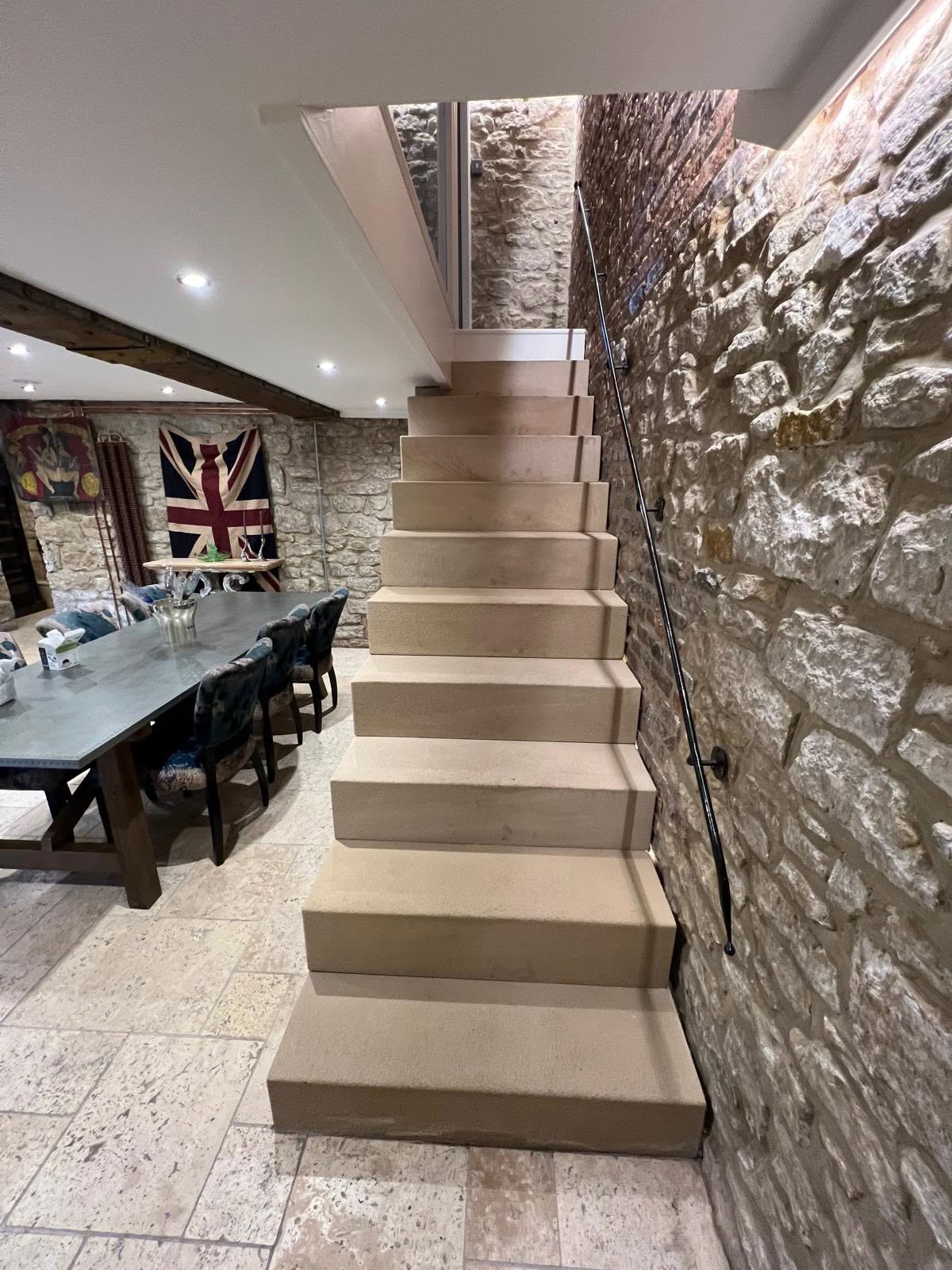 Cantilevered sandstone staircase head on with solid stone treads, slim black rod handrail and glass balustrade at the top