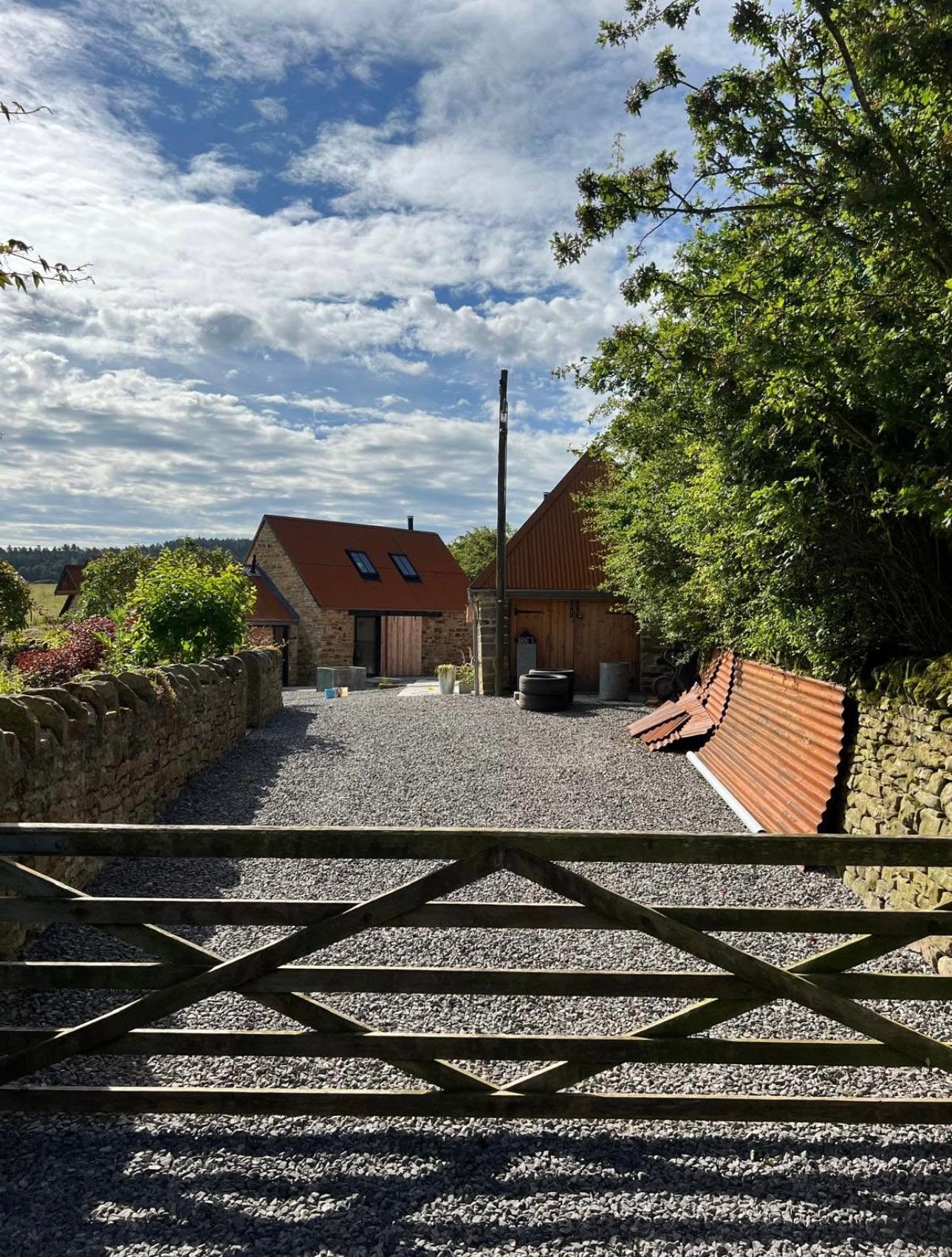 Approach from the field gate showing completed barns, corten style roofs and dry stone boundary wall