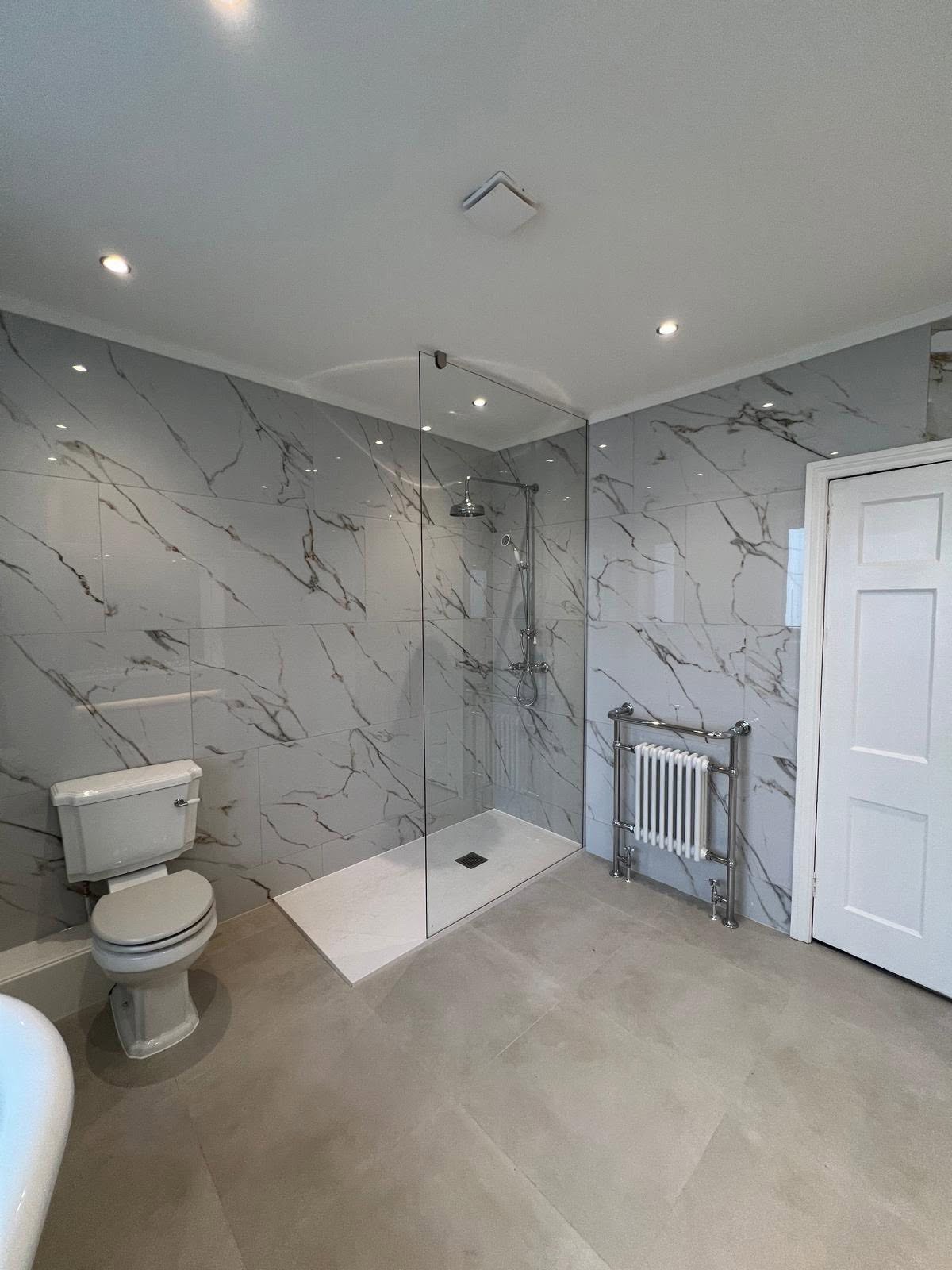 Glass enclosed walk in shower with marble effect tiling and chrome towel radiator