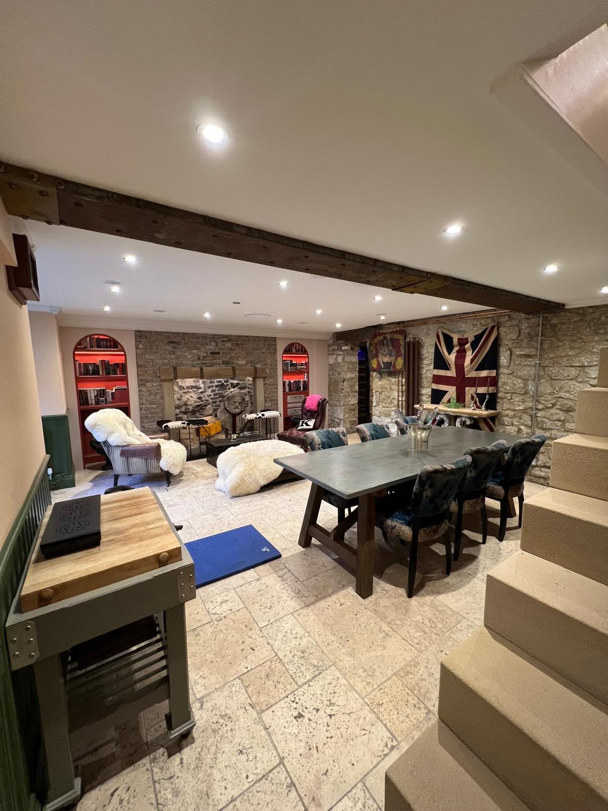 Full basement view from stone staircase showing dining zone, lounge zone, exposed stone wall and green panelled wainscot