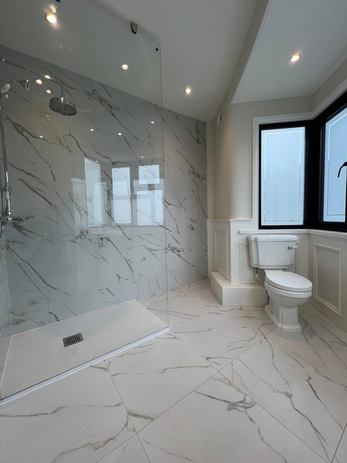 Walk in shower with seamless glass partition and large marble effect wall and floor tiles